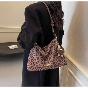 Detail of leopard print tote bag with brown plush pendant and decorative shoulder strap