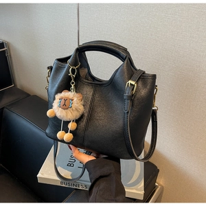 Detail of black lychee grain leather handbag with gold hardware and lion plush charm