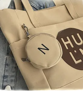 Detail of beige canvas tote bag with hanging round coin purse and brown leather patch