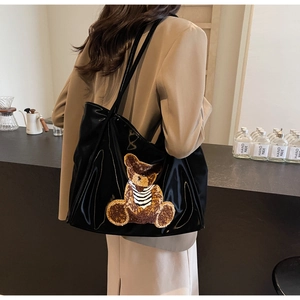 Detail of glossy black patent leather tote bag with a cute striped plush bear patch