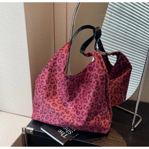 Detailed view of pink leopard print tote bag with black leather straps on a wooden table