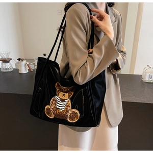 Close-up of a large black tote bag featuring an embroidered bear with striped shirt detail