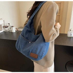 Detailed view of dark blue denim hobo bag featuring brown leather logo and silver rivets