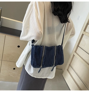 Detail view of deep blue denim crossbody bag featuring two parallel vertical zipper pockets