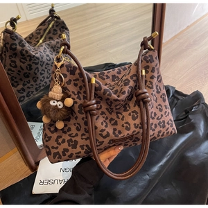 Detail of leopard print tote with knotted leather handles and plush monkey charm on silk