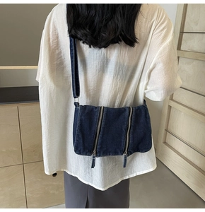 Detail view of denim crossbody bag with dual vertical zippers and adjustable strap