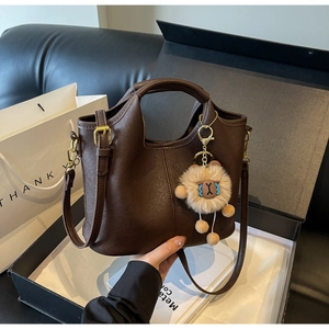 Detail of dark brown tote bag with plush lion charm in a gift box with a long strap