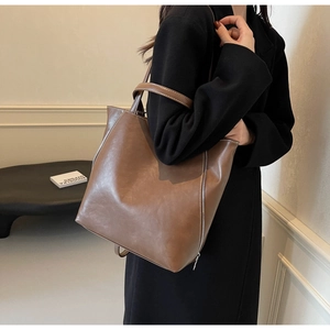 Close-up of brown leather tote bag featuring contrast stitching and side zipper details