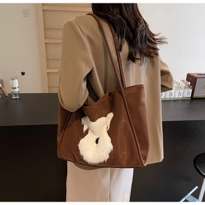 Detail of a brown large tote bag with a white plush puppy patch and slim shoulder straps