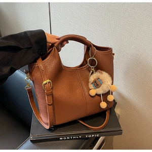 Detail of vintage brown tote bag with plush monster charm and adjustable shoulder strap