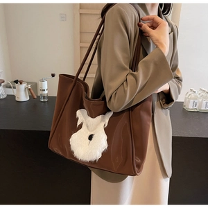 Detail of brown leather tote bag featuring a white fluffy dog patch and shoulder straps