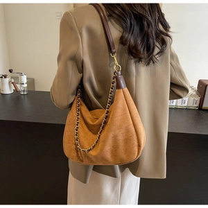 Detail of caramel suede hobo bag with chunky gold chain and brown leather strap on model