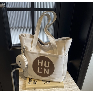 Detail of beige canvas tote featuring a leather logo patch and a mini round coin purse