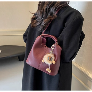 Close-up of wine red leather tote bag with plush charm on black coat background