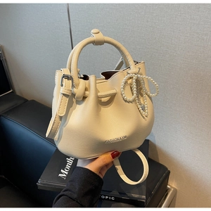 Detail der cremefarbenen Beuteltasche mit Perlenanhänger und verstellbarem Riemen