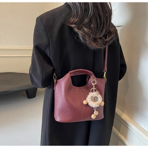Detail of burgundy crossbody bag with detachable strap and plush charm on black coat