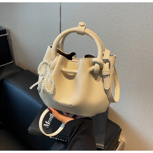 Detail der cremefarbenen Beuteltasche mit Perlen-Schleife und verstellbarem Gurt