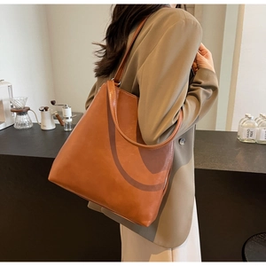 Detail view of large caramel tote bag with slender straps and side zipper on a model