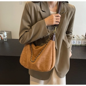 Detail of caramel suede crescent bag with gold chain strap on a model wearing a blazer