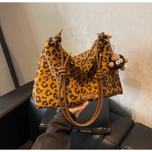 Close-up of leopard print tote bag with brown leather handles and monkey plush charm