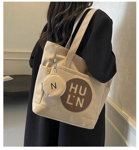 Close-up of beige canvas tote bag with embossed HULN logo and round coin purse charm