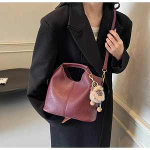 Detail of burgundy leather tote bag with vertical stitching and cute plush charm pendant