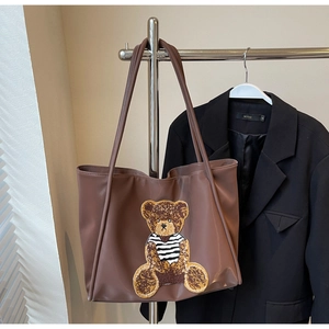 Detail of a large brown tote bag featuring a cute fuzzy bear patch in college style