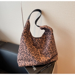 Close-up of leopard print tote bag with black handles leaning on leather and magazine