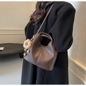 Detail of dark brown faux leather tote with lion plush charm and vertical stitching details