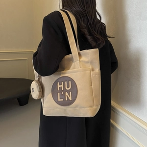 Detail view of beige canvas tote with brown leather logo patch and round pouch accessory