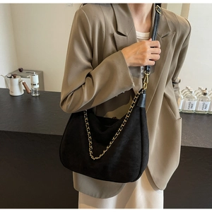 Detail of matte black shoulder bag with gold chain and adjustable strap on model