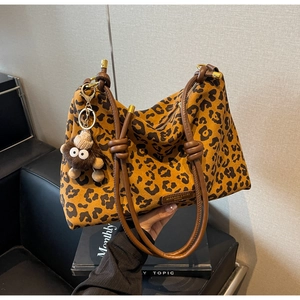 Close-up of leopard print tote bag with brown leather handles and a plush doll pendant