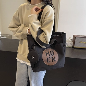 Detail of black canvas tote bag with circular leather logo patch and matching small coin purse