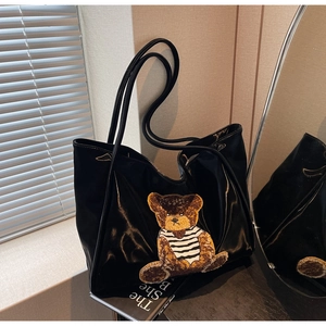Close-up of black tote bag featuring a plush teddy bear patch and shiny material finish