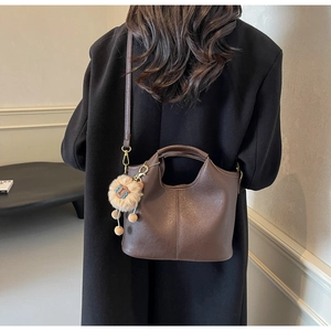 Detail of dark brown leather tote bag with plush lion charm and adjustable strap