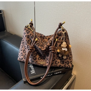 Detail of leopard print tote bag featuring leather straps and a cute plush doll charm