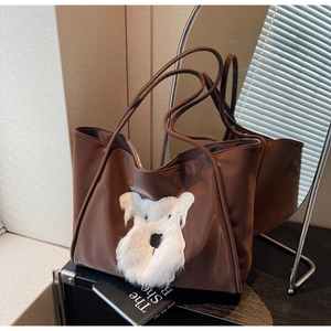 Detailed close-up of a brown tote bag with white plush animal patch and dual straps