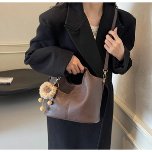 Detail of dark brown leather tote with decorative stitching and plush lion charm