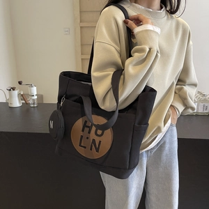 Detail shot of black canvas tote bag with brown leather logo patch and mini coin purse