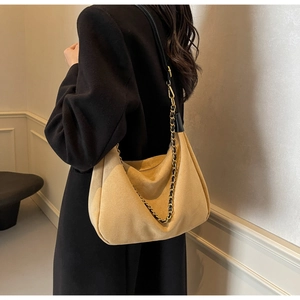 Detail of light brown suede hobo bag with a gold and black chain strap on a model