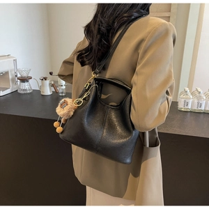 Detail of black faux leather tote with plush charm and vertical stitching in a cafe setting