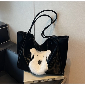 Detail of black tote bag featuring a fluffy white dog plush patch on glossy material