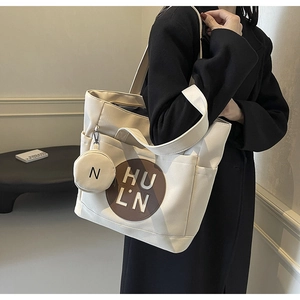 Close-up of cream canvas tote bag with brown letter logo patch and mini coin purse charm