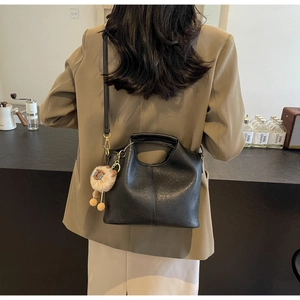Detail of black faux leather tote bag with plush sheep charm worn by model in a cafe