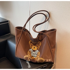 Close-up of a brown leather tote bag featuring a 3D plush bear embroidery detail