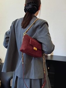 Chic burgundy quilted suede shoulder bag with gold chain strap on a stylish woman