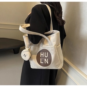 Detail of white canvas tote bag featuring brown logo patch and detachable coin purse