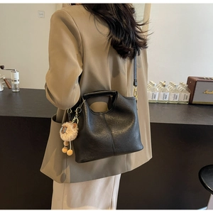Model wearing black leather tote bag with a soft sheep wool charm in a cafe setting