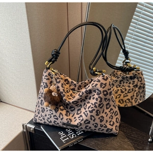 Detail of leopard print tote bag with black rope handles and brown plush charm accessory