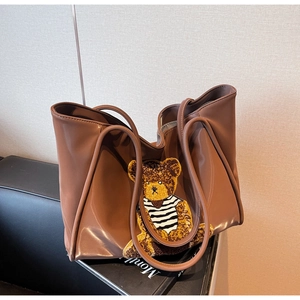 Detail of a brown faux leather tote bag featuring a teddy bear embroidery patch
